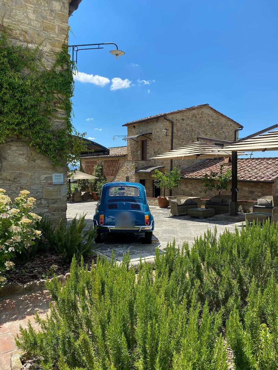 A vintage Fiat 500 in the courtyard of a stone farmhouse